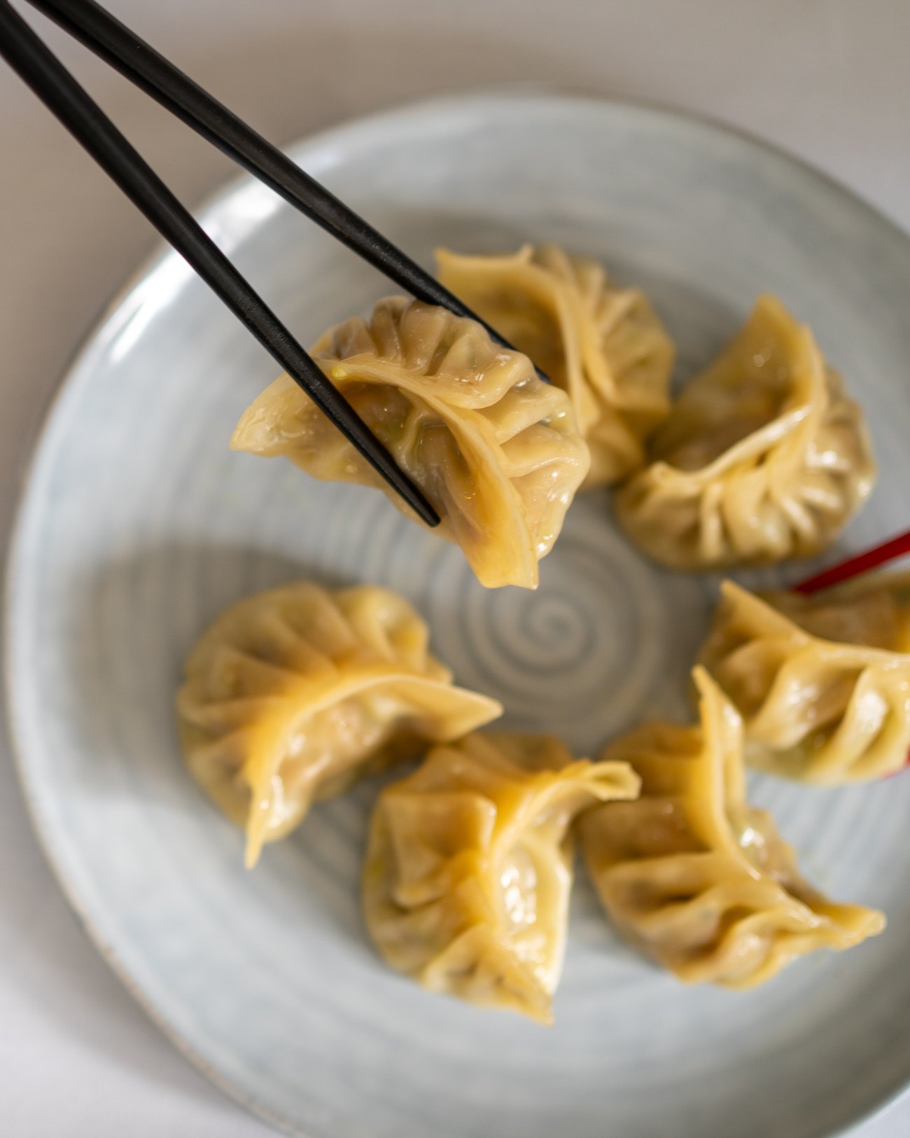A dumpling lifted with chopsticks above a plate of handmade dumplings
